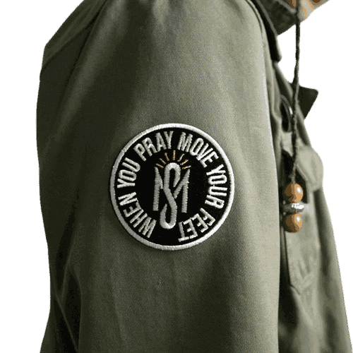 Custom circular embroidered patch attached to the sleeve of an olive green jacket featuring an interlocking logo surrounded by the text 