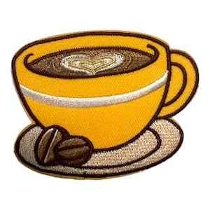 Custom embroidered coffee cup patch featuring a yellow teacup with heart latte art resting on a saucer alongside two dark coffee beans.
