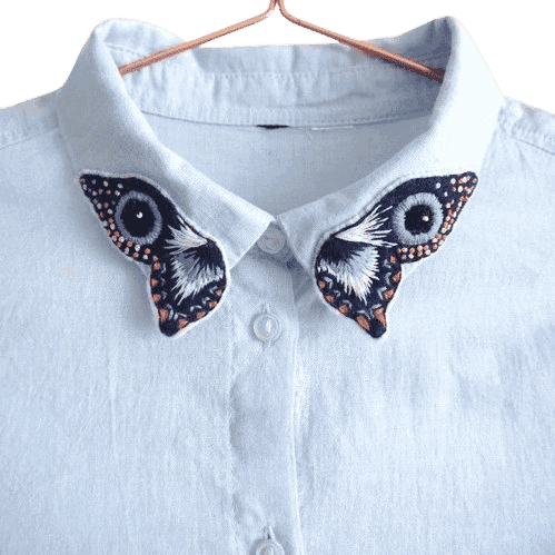 Custom embroidered moth wing collar patches attached to the collar tips of a white button-up shirt displayed on a hanger.