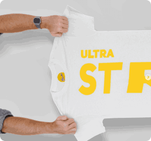 Custom apparel mockup featuring a pair of hands holding up a white t-shirt printed with bold yellow typography reading 