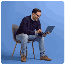 A professional man sitting on a chair working on a laptop computer in a studio setting.
