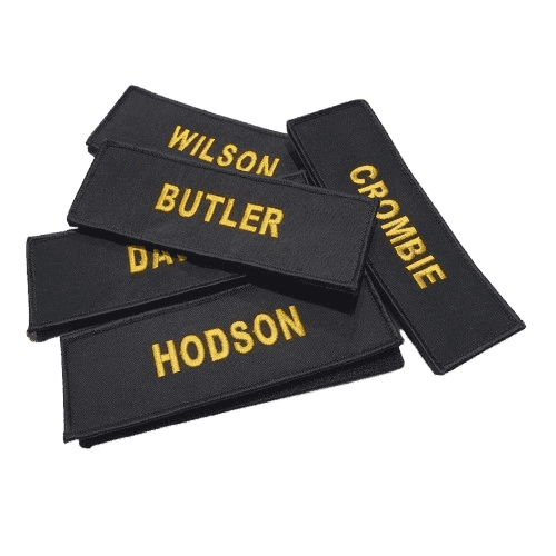 Custom embroidered black rectangular name patches featuring bold orange text with the names Wilson, Butler, Crombie, and Hodson on a transparent background.
