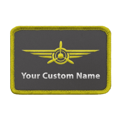Custom woven rectangular name patch featuring a dark grey background, a yellow winged propeller aviation emblem, a yellow border, and a placeholder reading 