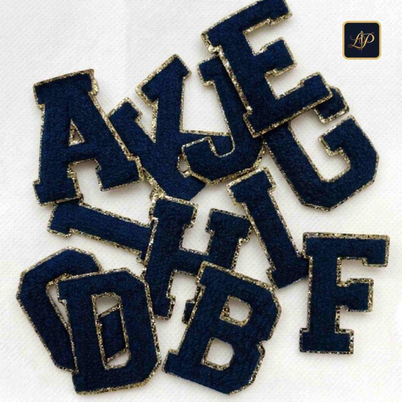 Navy blue and gold varsity chenille letter patches stacked on fabric.